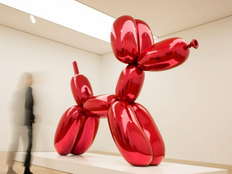 Image of the art piece called Balloon Dog (a giant red dog made of balloon) in a museum.