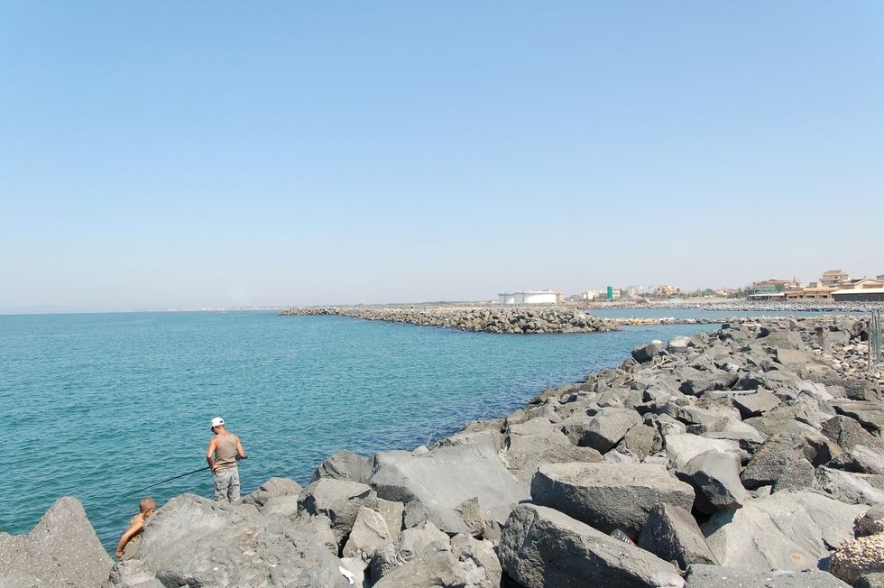 Image of two men, one fishing in the sea, in the city of Fiumicino.