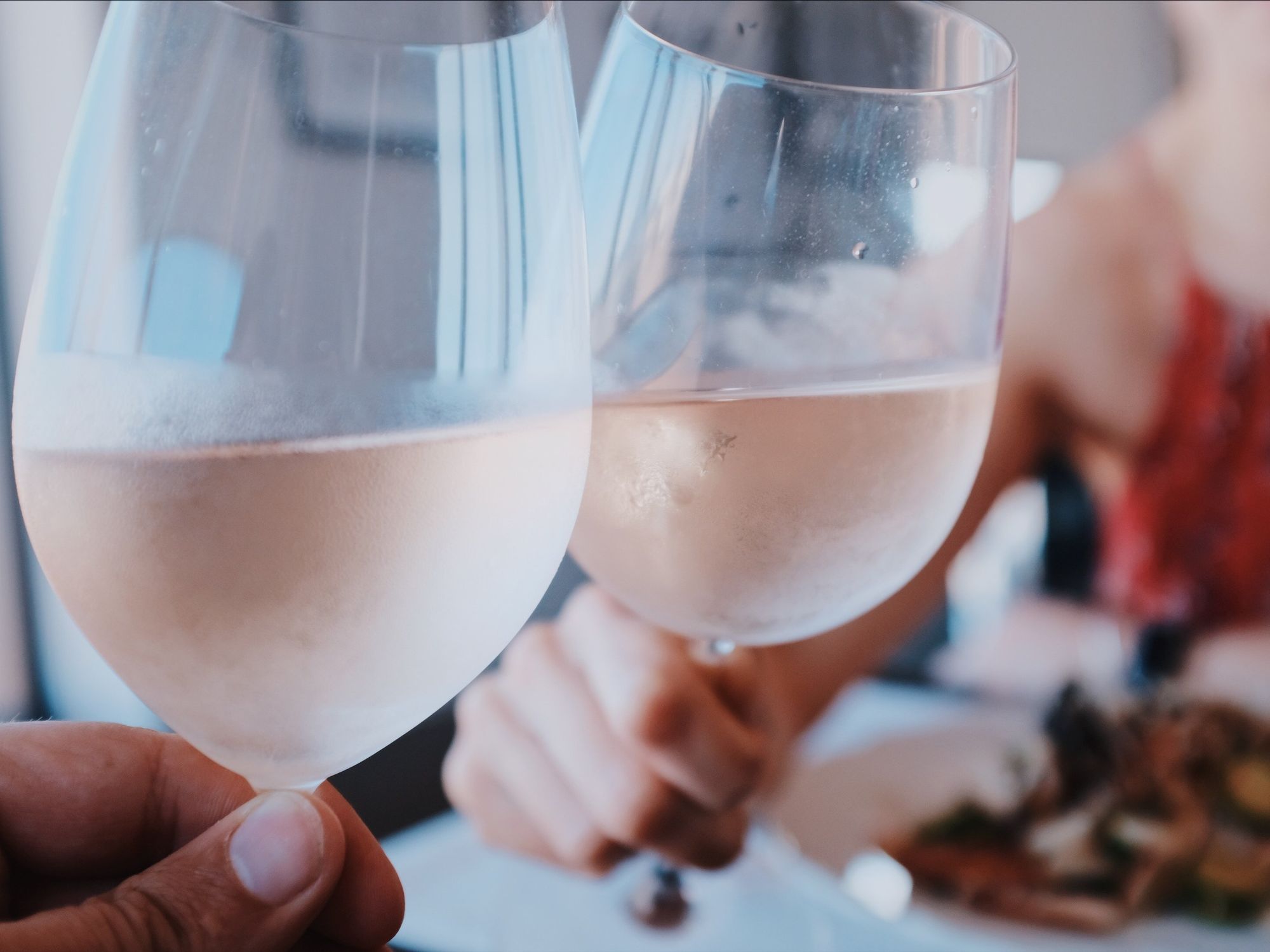Image of two people cheering with wine glasses filled with rosé wine.