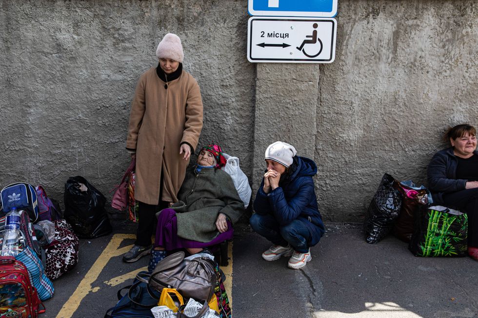 Image of two sisters along with their mother, luggage on the floor, waiting for an emergency evacuation bus
