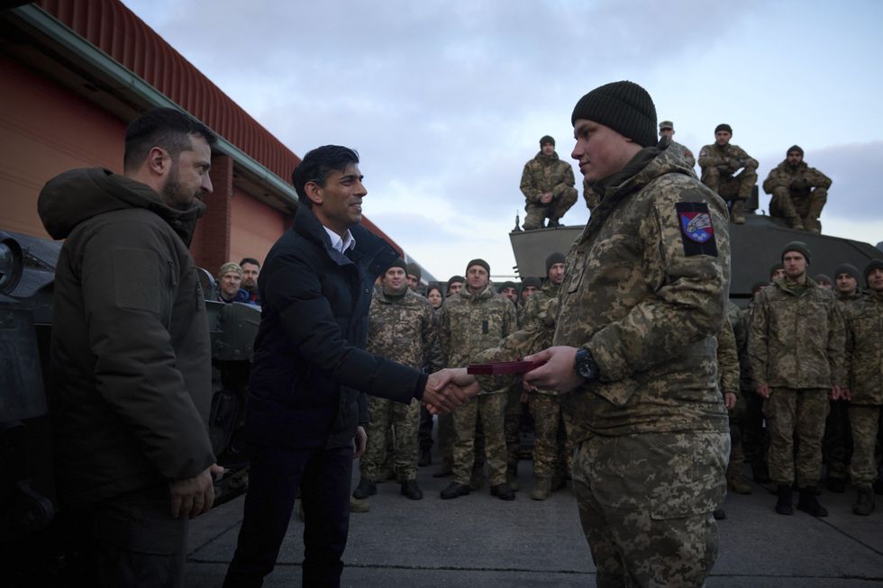 Image of Ukrainian President Volodymyr Zelenskyy, left, presenting service medals to Ukrainian soldiers as British Prime Minister Rishi Sunak, center, offering congratulations during a visit to Bovington Camp Armour Centre, February 8, 2023 in Dorset, United Kingdom.