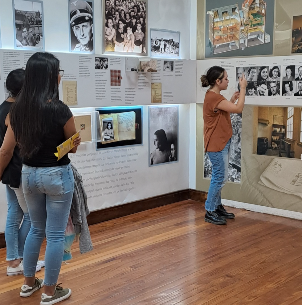 Image of visitors visiting the Anne Frank center in argentina, the walls of the room are covered with pictures of Anne Frank and documents about her life,
