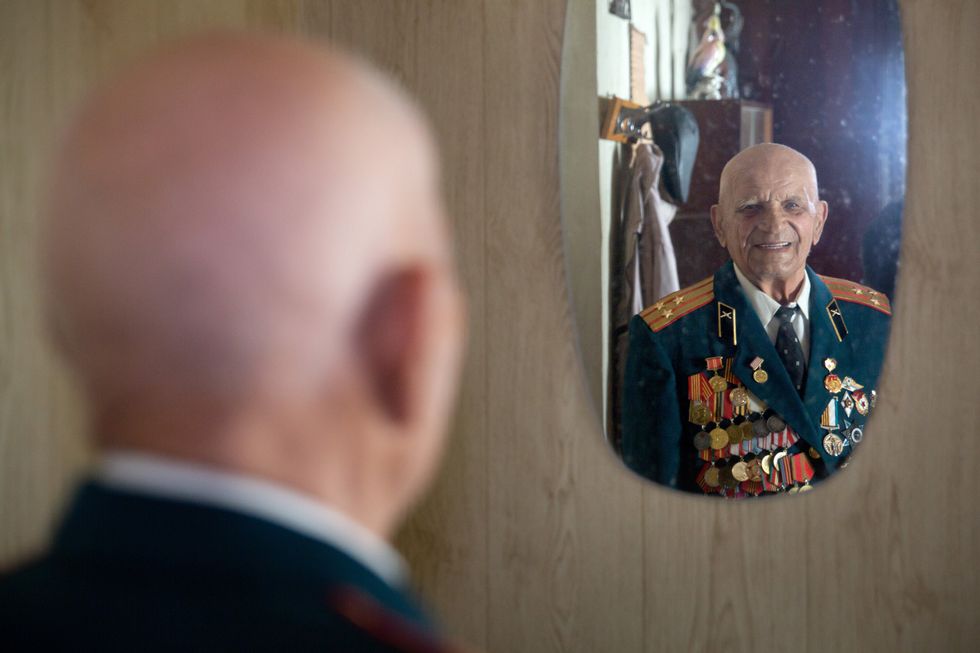 Image of WWII veteran Pavel Kutovoi looking at himself in a mirror in his apartment in Lugansk, Ukraine.