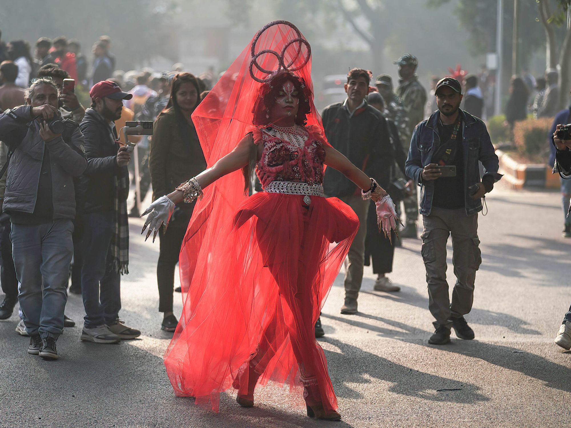 Image showing a drag queen taking part in New Delh's Queer Pride Parade. She wears a red gown that flows behind her as she walks.