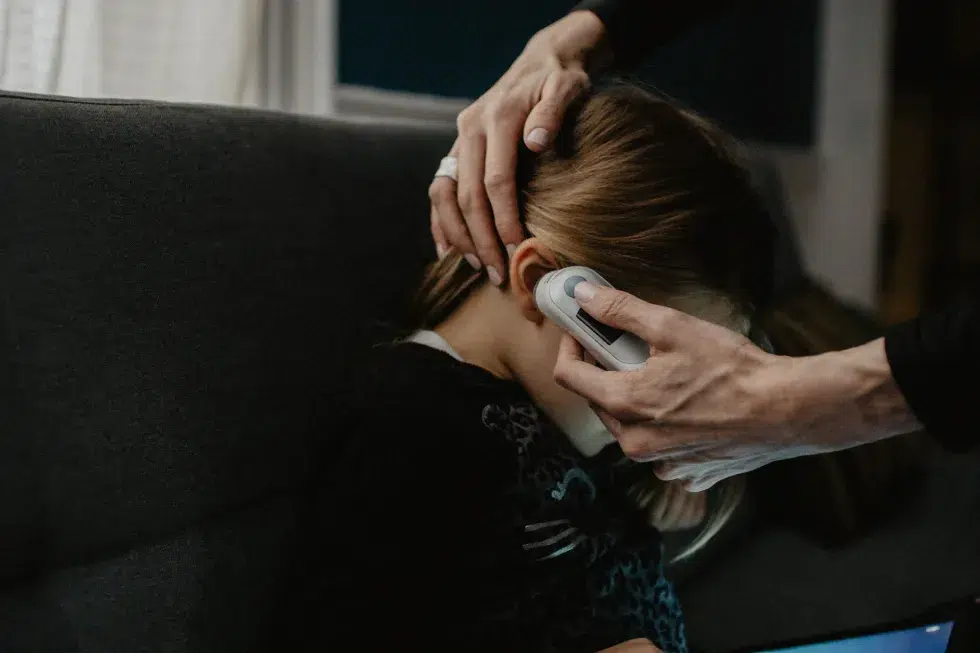 image showing a ​mom taking the temperature of her daughter with an ear thermometer