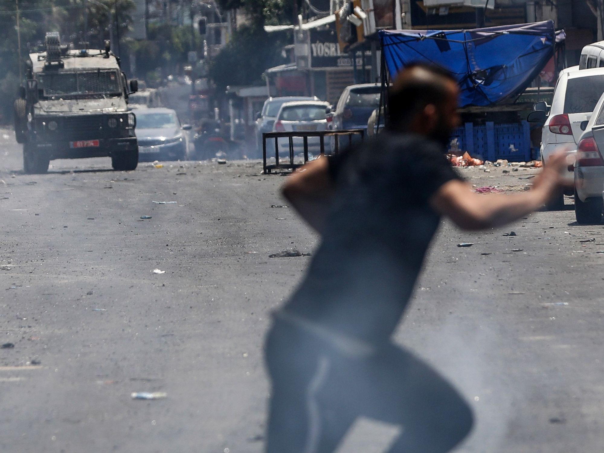 Image showing a Palestinian man running as Israeli military vehicles fire tear gas near the eastern entrance to the Jenin refugee camp