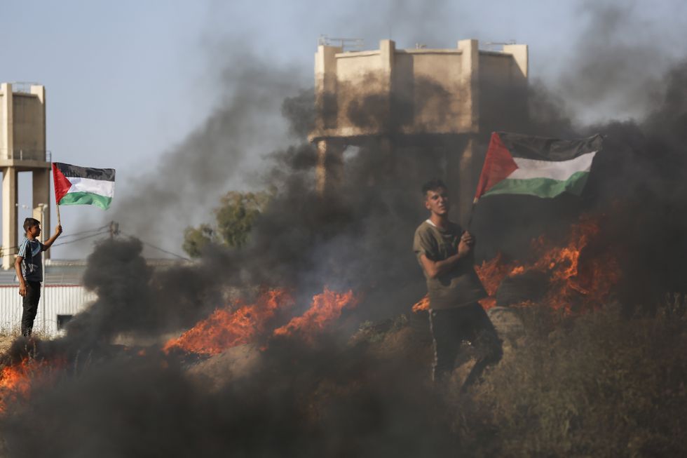 Image showing Palestinian youths holding flags near burning tires during the protest against Israeli military operations in Jenin.