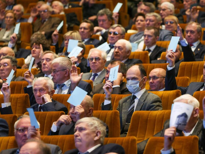 In an auditorium, members of the Russian Academy of Sciences raise papers to vote
