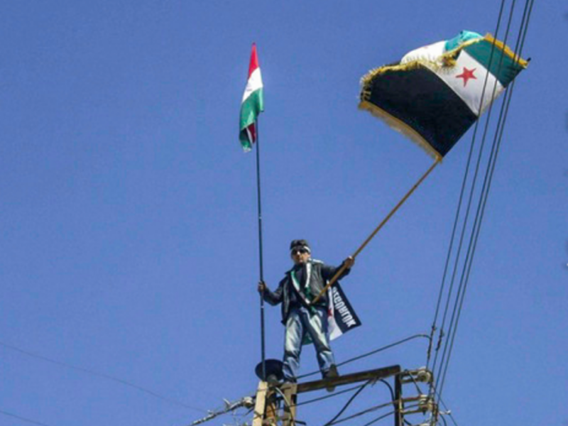 In the Syrian border town of Qamishli, a protester with a Kurdish and Syrian rebel flag (Freedom House)