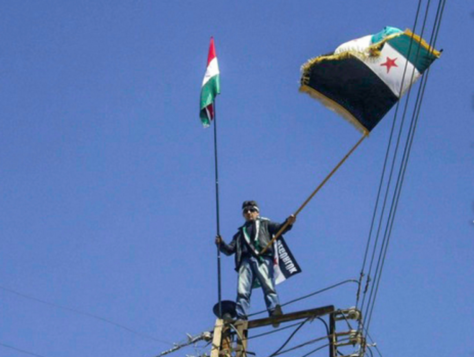 In the Syrian border town of Qamishli, a protester with a Kurdish and Syrian rebel flag (Freedom House)