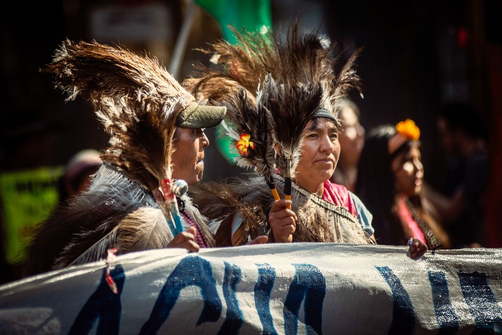 Indigenous protesters in regalia march while holding feathers and a banner
