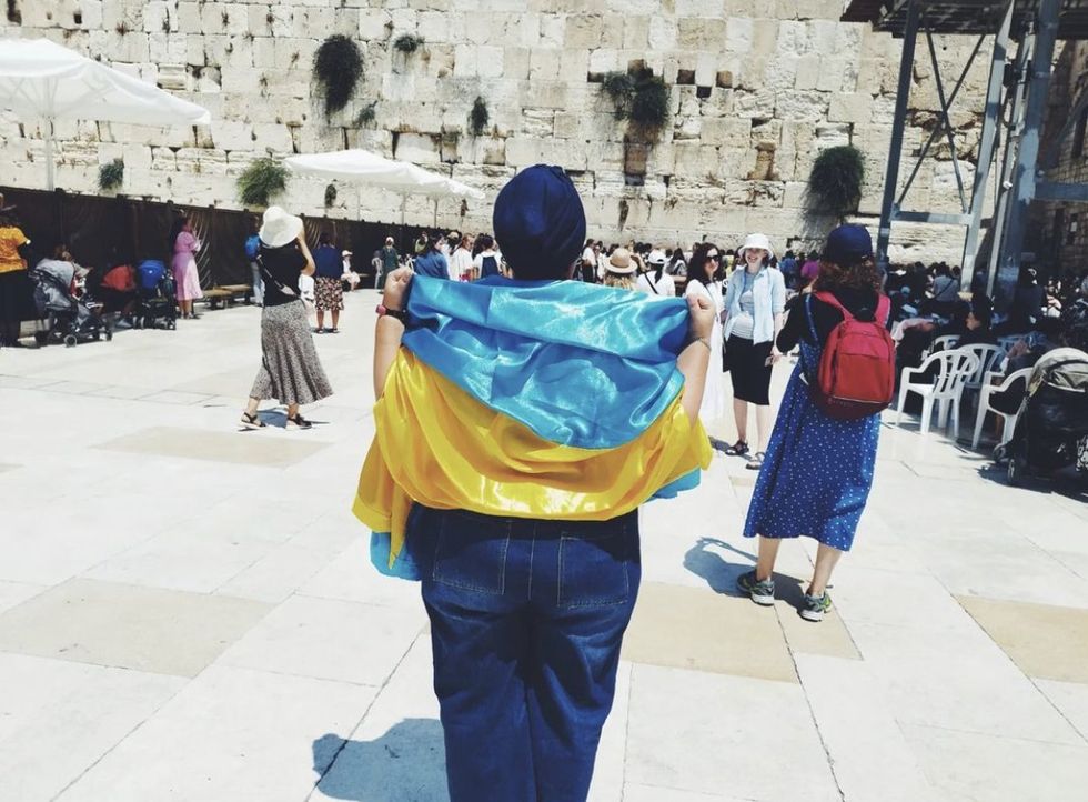 Inna stands with her back to the camera at Temple Mount, a Ukrainain flag over her shoulders
