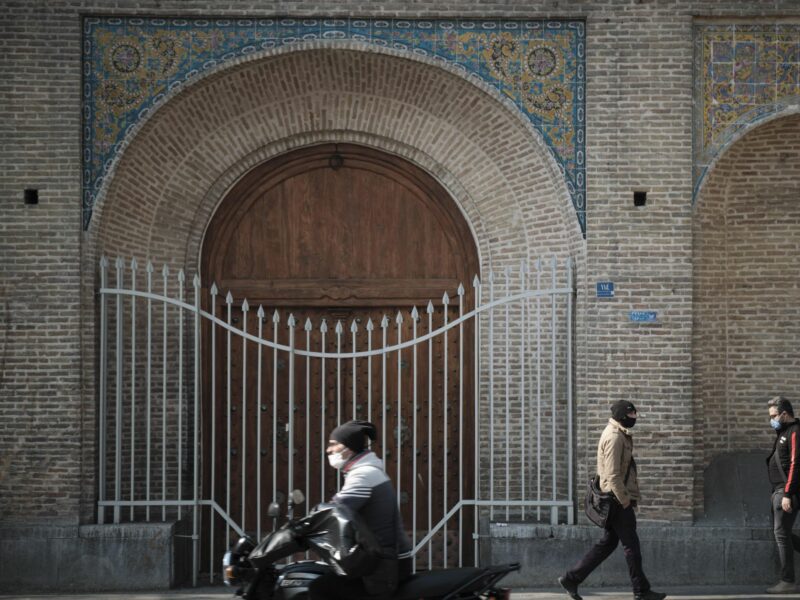 Iranian men wearing protective face masks walk along a street-side near Tehran's Traditional Grand bazaar