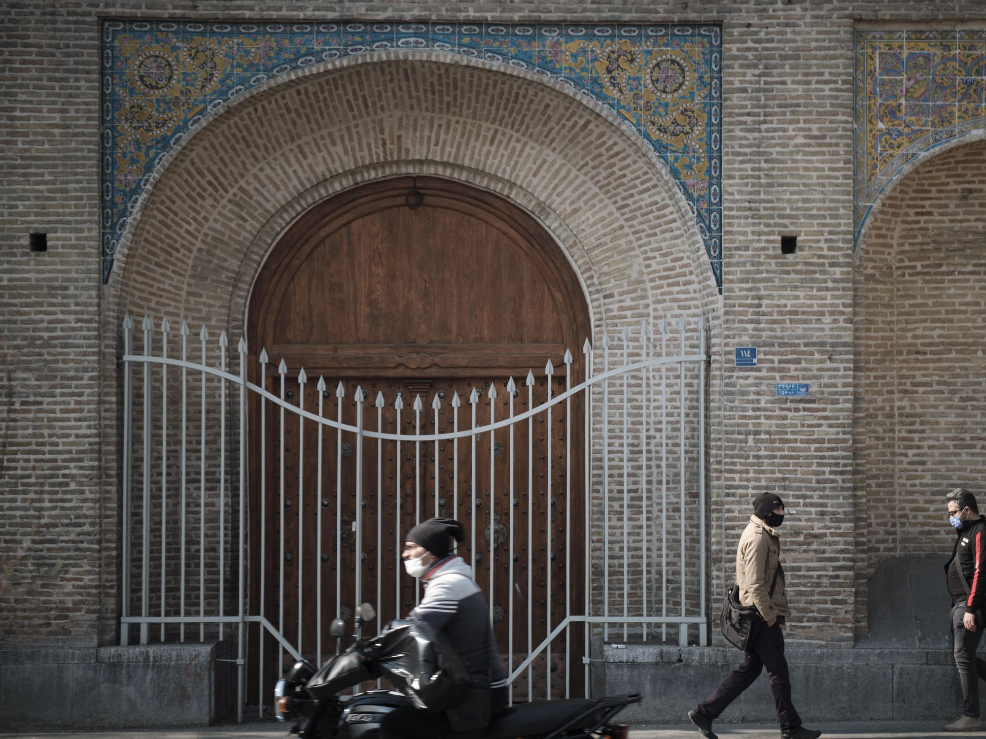 Iranian men wearing protective face masks walk along a street-side near Tehran's Traditional Grand bazaar