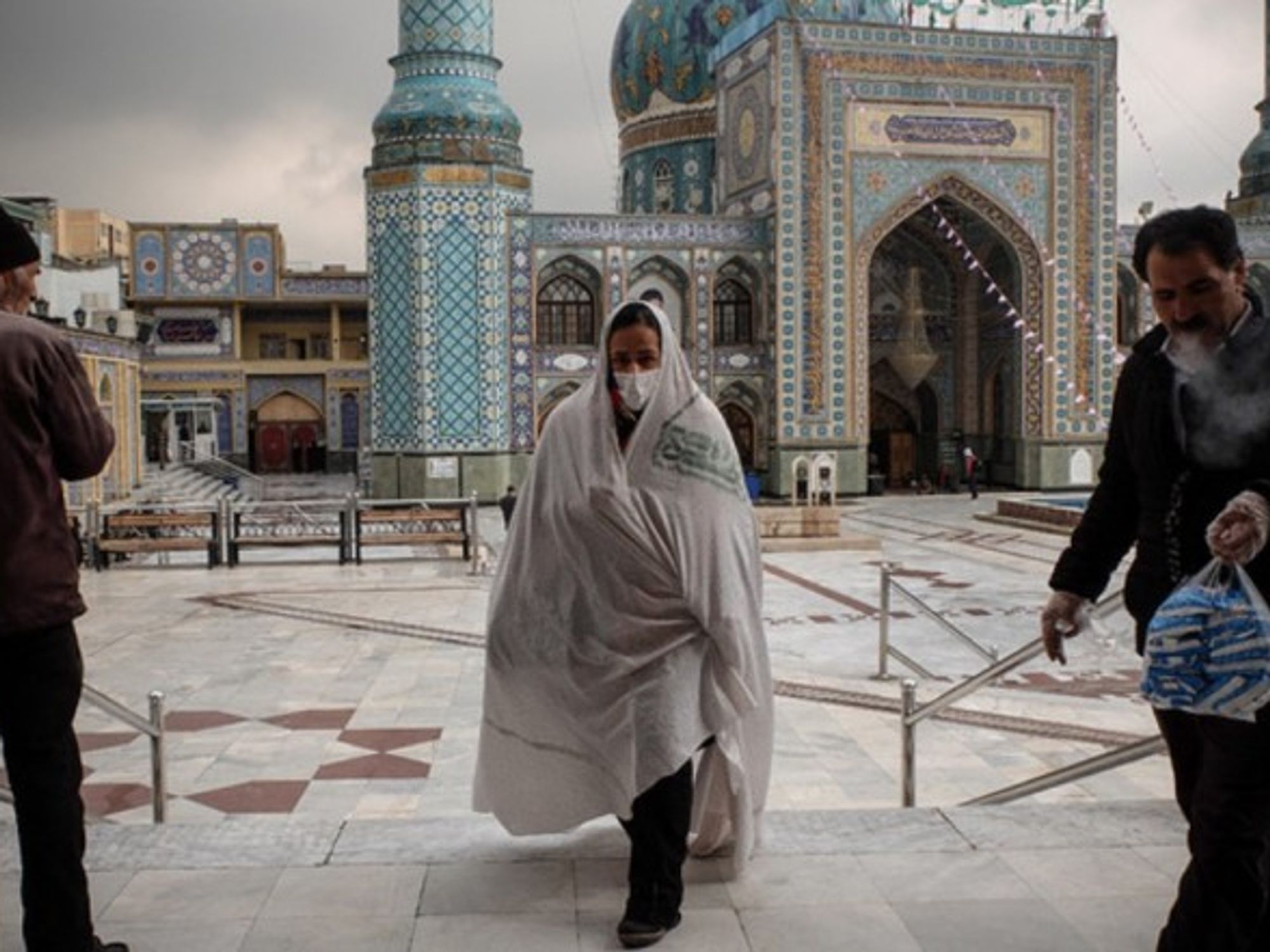 Iranians wearing face masks walk past a mosque in Tehran.