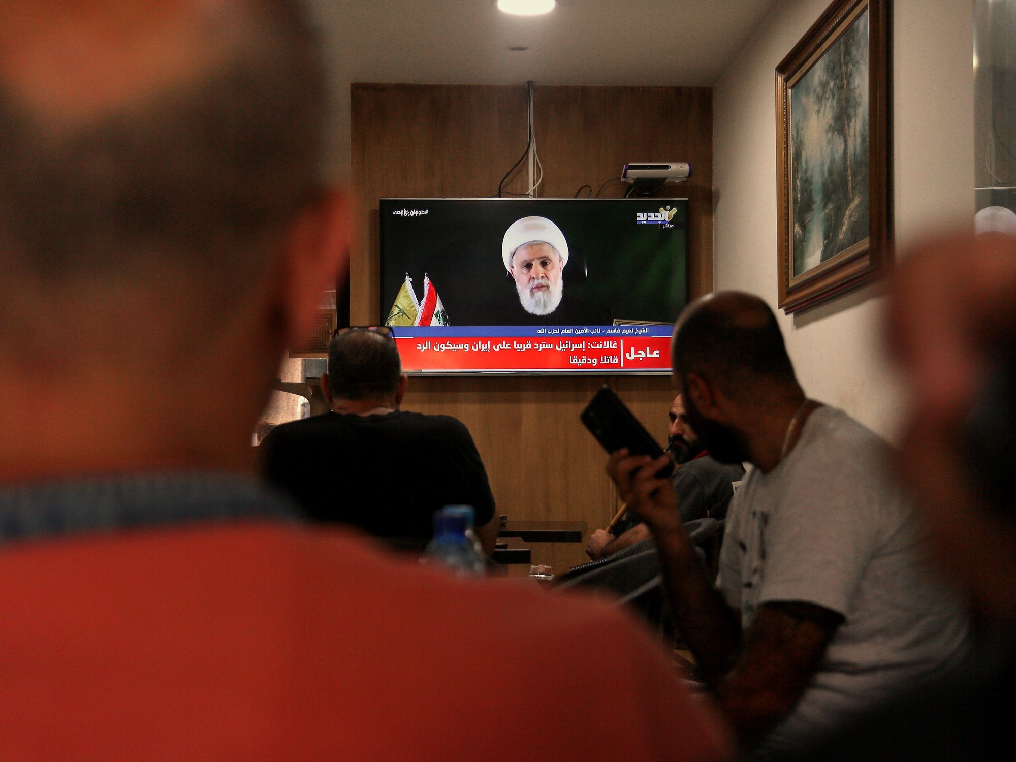 Lebanese citizens in a café in Beirut watching a televised speech by Naim Qassem.
