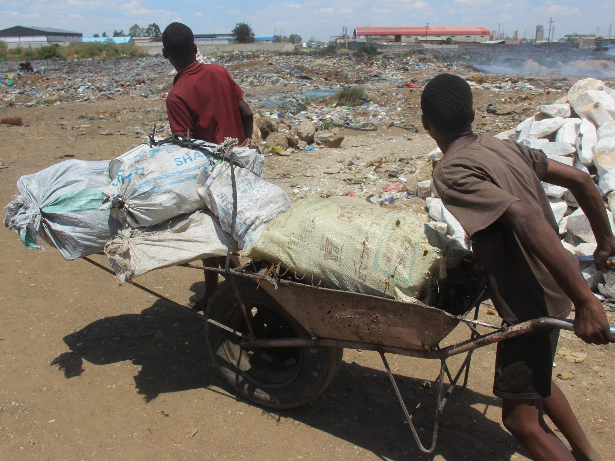 Luke, 13, left, and his brother Oswald, 17, steer a wheelbarrow full of metal bars they scavenged at the Marabo garbage dump in Lusaka, Zambia.