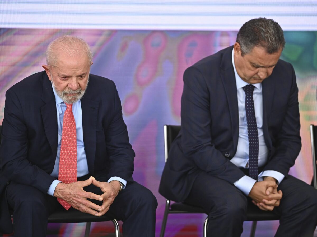Lula Da Silva sits in a chair on a stage, with his hands together looking sad
