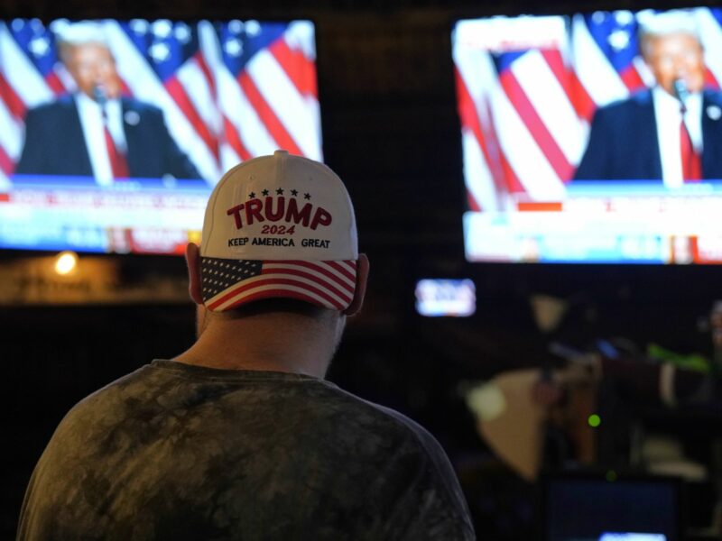 MAGA supporter watching TV newscast showing Donald Trump in Fort Lauderdale, Florida.