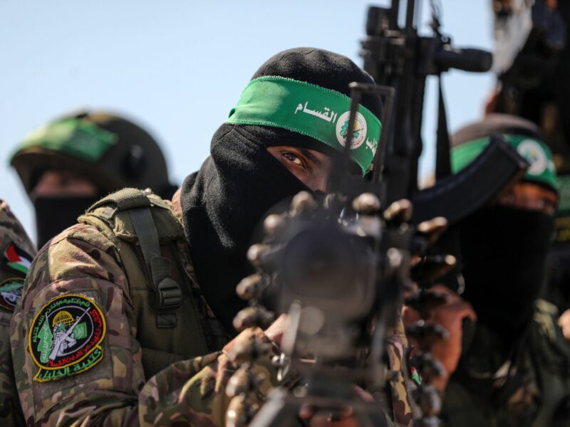 Man aiming a weapon at the camera with similarly dressed men surrounding him