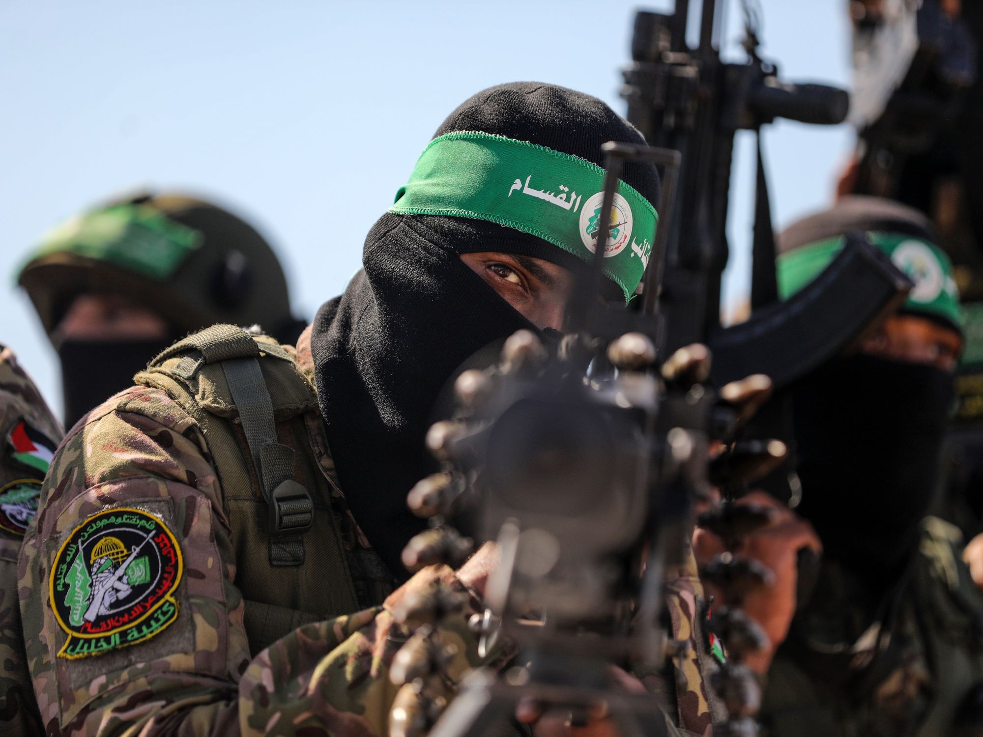 Man aiming a weapon at the camera with similarly dressed men surrounding him