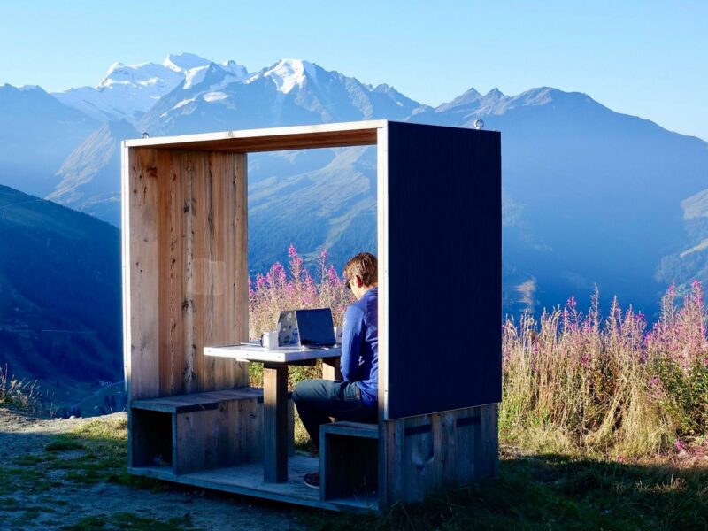 Man surronded by nature working in a wooden box on his laptop.​