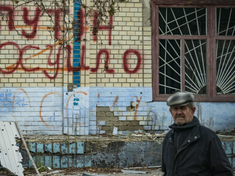 Man walking past an anti-Putin graffiti on a destroyed wall in