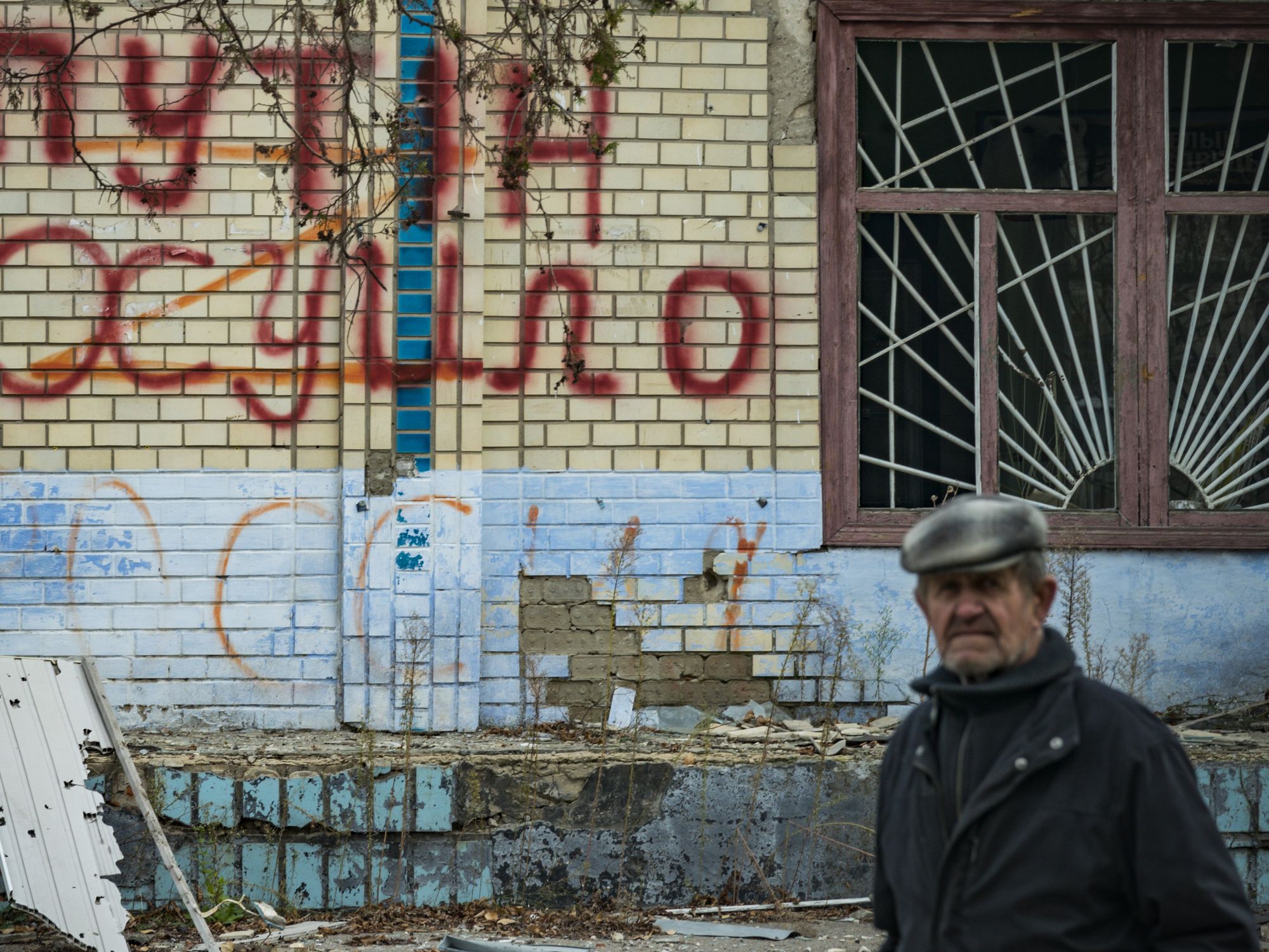 Man walking past an anti-Putin graffiti on a destroyed wall in