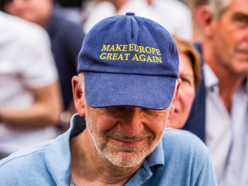 Man wearing a "Make Europe Great Again" hat sitting with a crowd