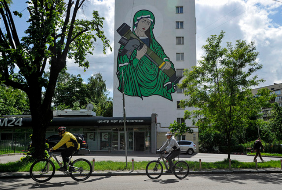May 2022, Kyiv, Ukraine: Cyclists ride past a residential building with a mural depicting ''Saint Javelin''.