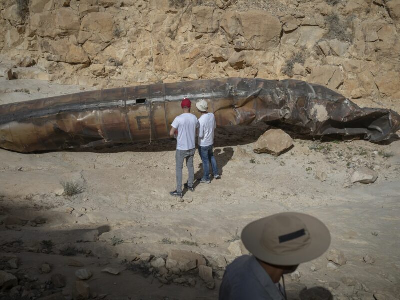 Members of military personnel in civilian clothing inspect apparent remains of a ballistic missile lying in the desert.