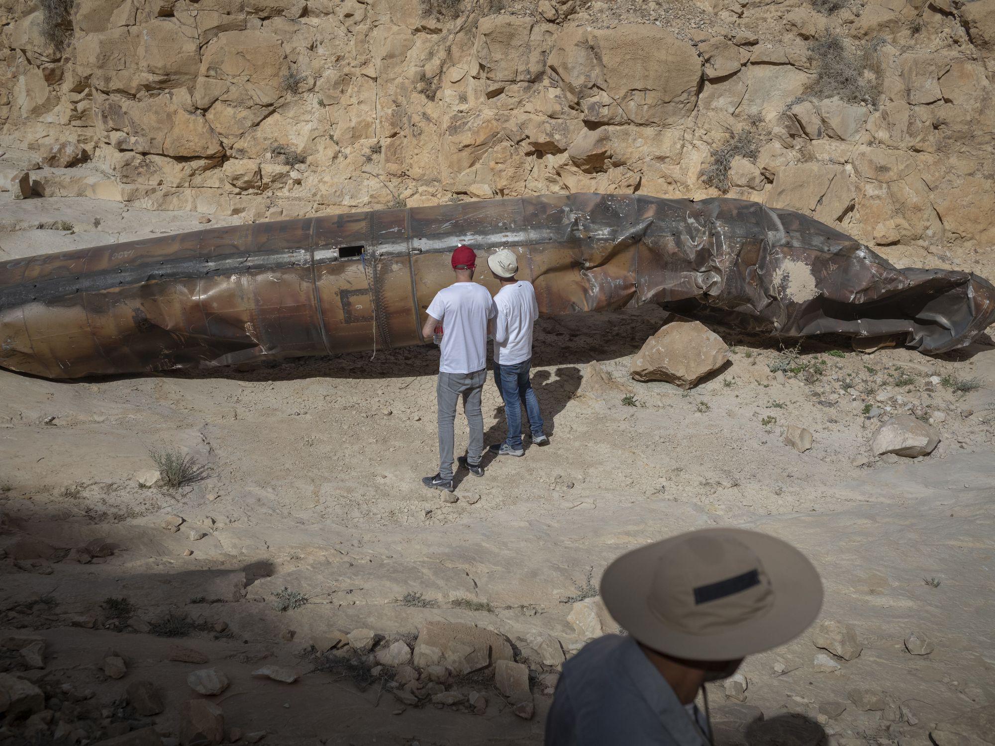 Members of military personnel in civilian clothing inspect apparent remains of a ballistic missile lying in the desert.