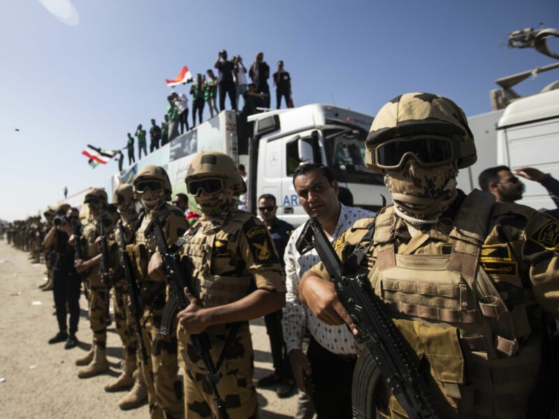 members of the Egyptian military, some with flags and guns, stand around and on top of transport vehicles.