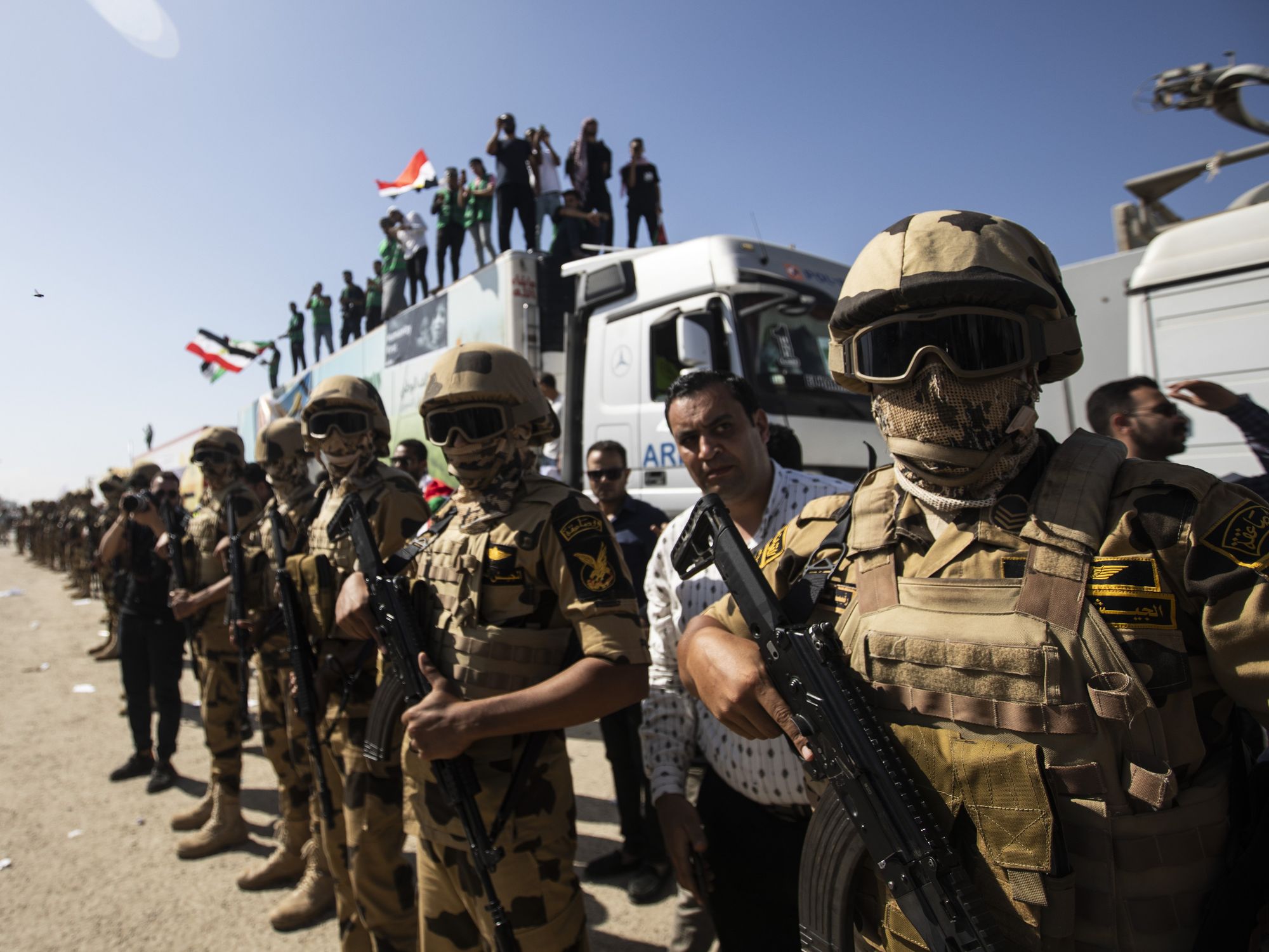 members of the Egyptian military, some with flags and guns, stand around and on top of transport vehicles.