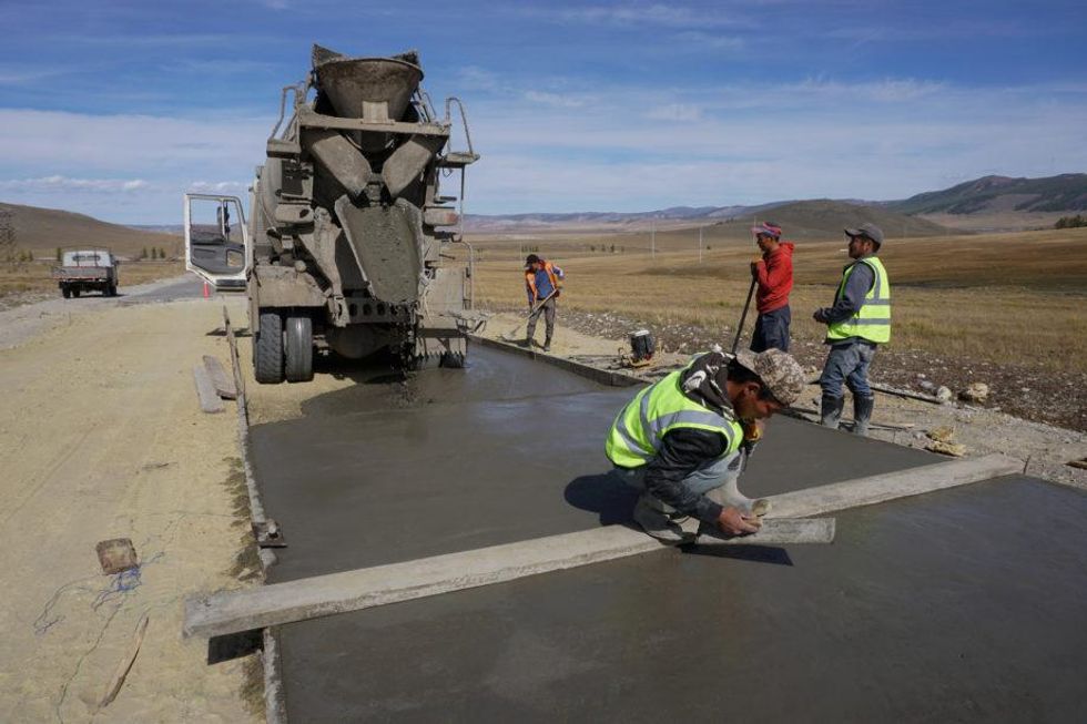 Men smoothening the fresh concrete on a road being built in Mongolia