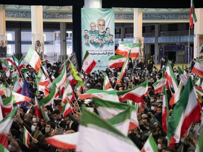 Men wave the Iranian flag in front of a poster of General Qasem Soleimani