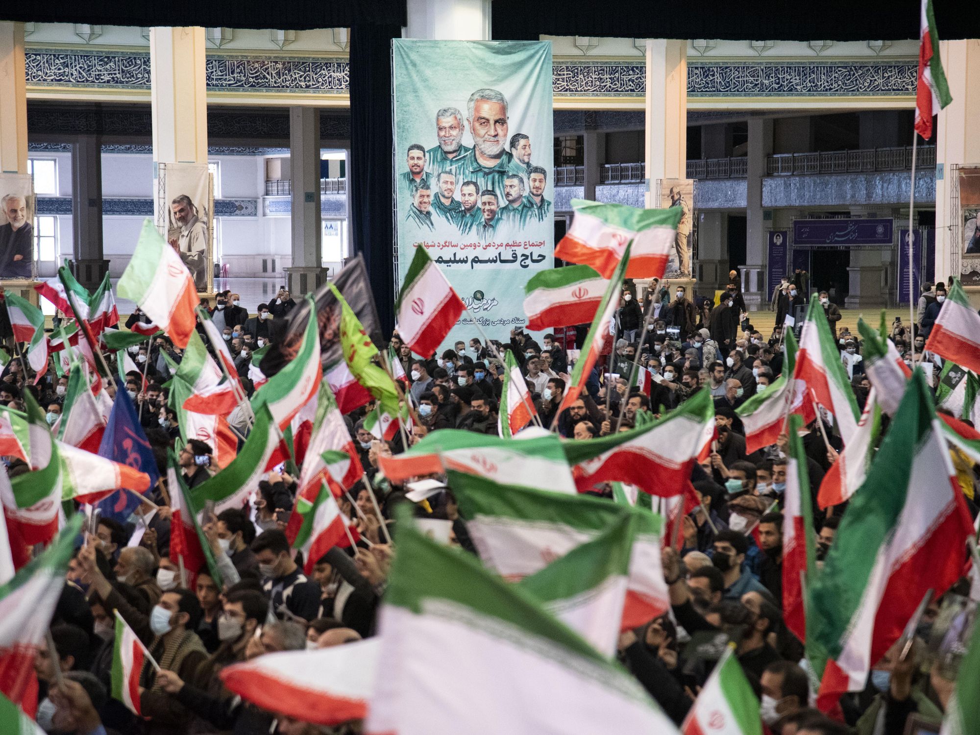 Men wave the Iranian flag in front of a poster of General Qasem Soleimani