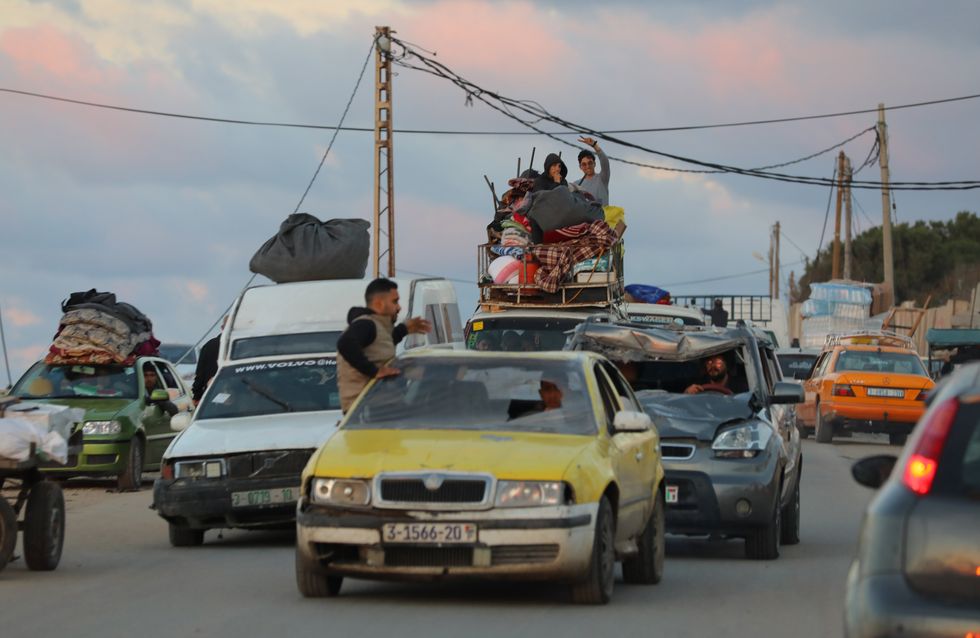 Palestinian families fleeing, theres a man hanging out of a yellow car with the windshield broken, a family on top of the car holding up the peace sign to the camera, and a severly damanged car.