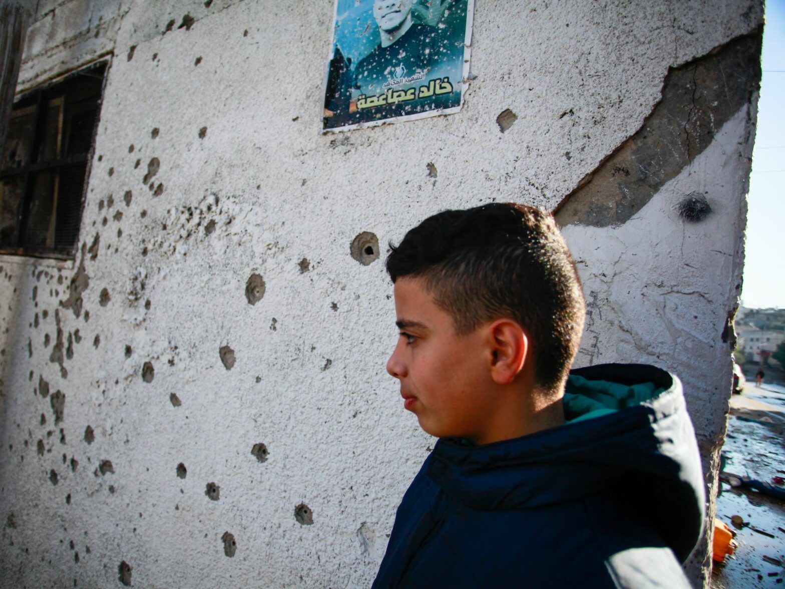 Palestinian kid next to a house riddled with bullet holes.