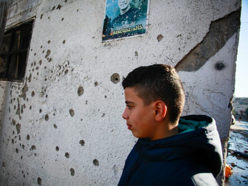 Palestinian kid next to a house riddled with bullet holes.