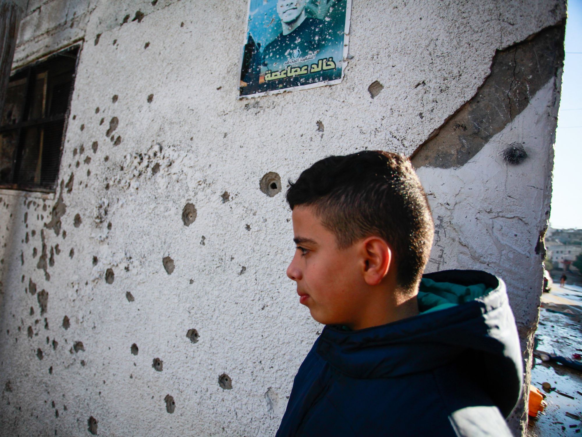 Palestinian kid next to a house riddled with bullet holes.