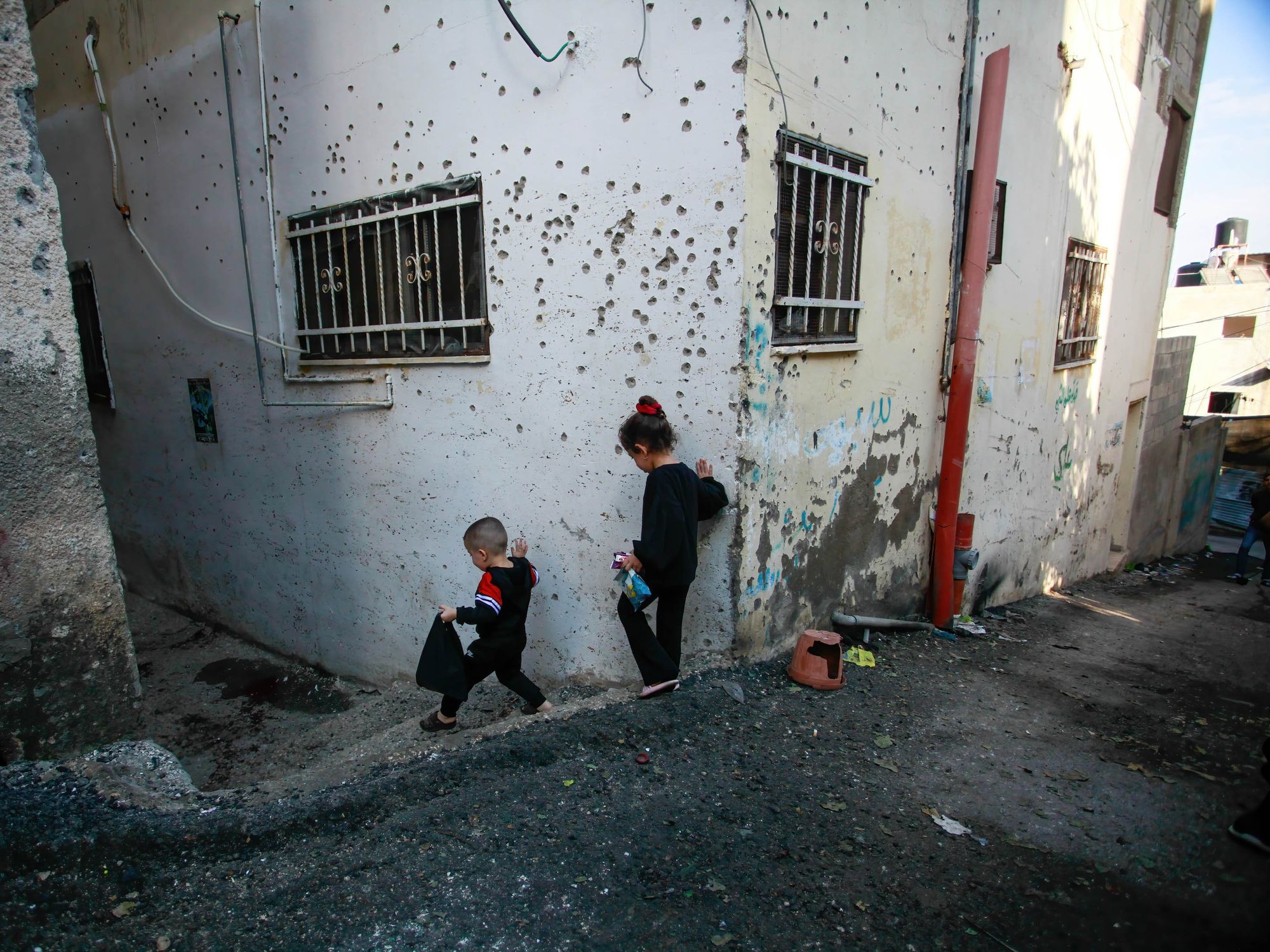 Palestinian kids walk by a damaged house following an Israeli military raid in Jenin refugee camp.