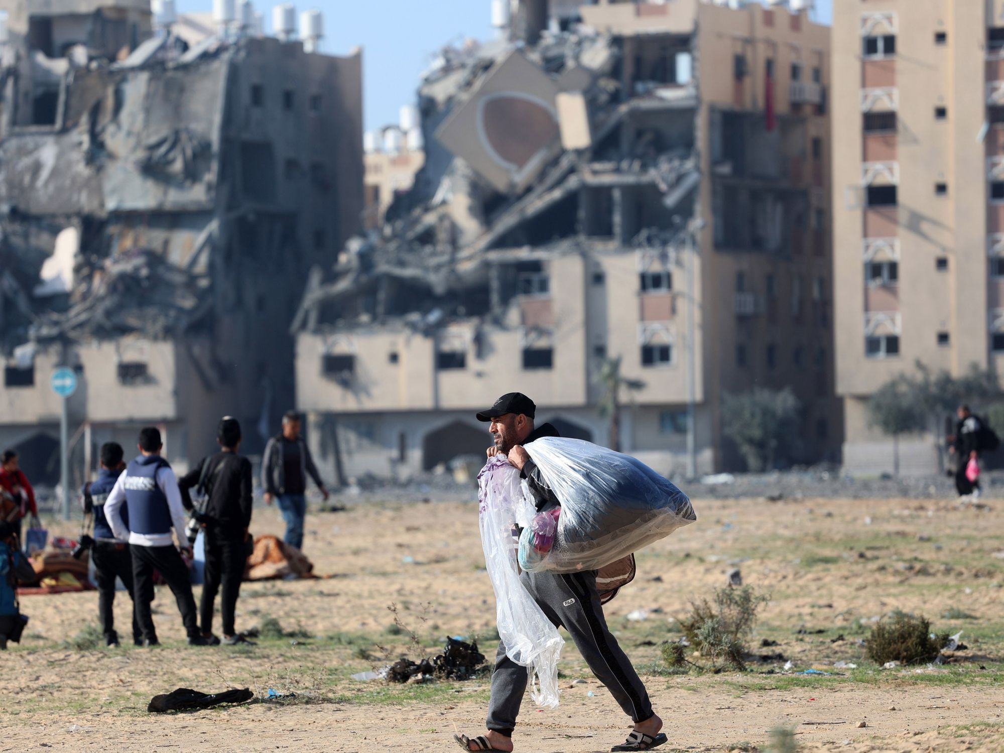 Palestinian man walks in front of the destroyed buildings as they flee their homes after an Israeli strike hit 7 towers in the city of Hamad.