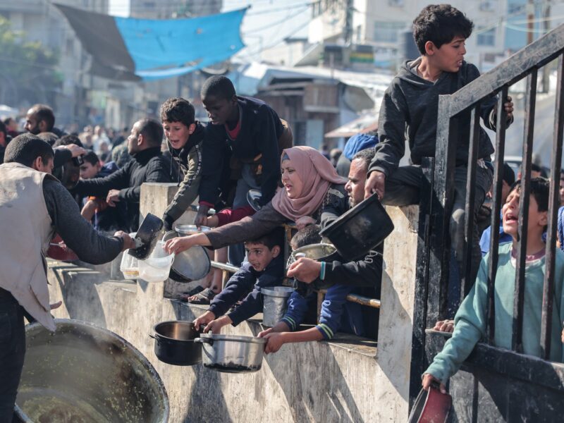 Palestinians gather with pots to receive food at a donation point provided by a charitable organization in Rafah.
