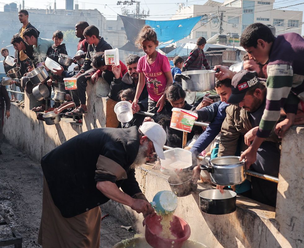 Palestinians gather with pots to receive food at a donation point provided by a charitable organization in Rafah in the southern Gaza Strip