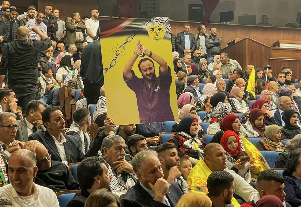 Palestinians sit at a ceremony marking the 21st anniversary of the arrest jailed Fatah leader Marwan Barghouti. A man carries his photo .