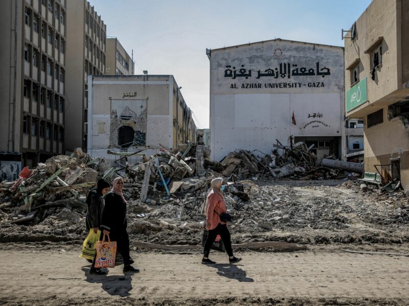 Palestinians walk next to the remaining of Al-Azhar University's building.