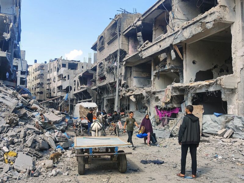 Palestinians walk on the street filled with debris of destroyed buildings.