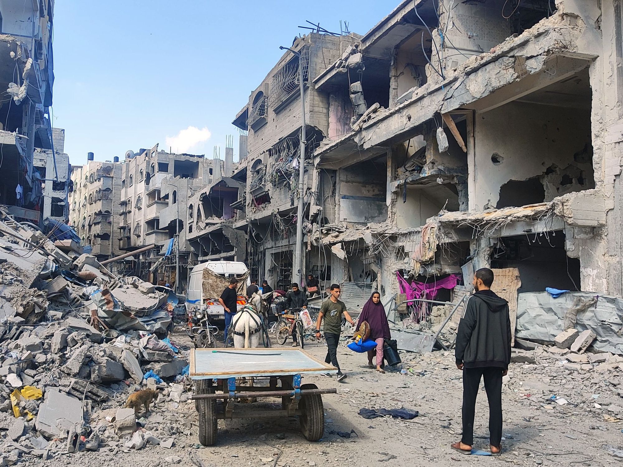 Palestinians walk on the street filled with debris of destroyed buildings.