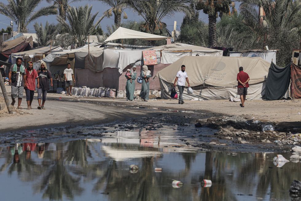 Palestinians walks near tents used as shelter along a street covered with stagnant wastewater in Deir el-Balah in the central Gaza Strip on July 22, 2024.